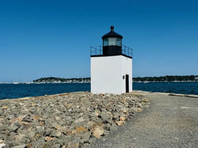 Small white lighthouse with a black top standing on a rocky path along the ocean at Derby Wharf.