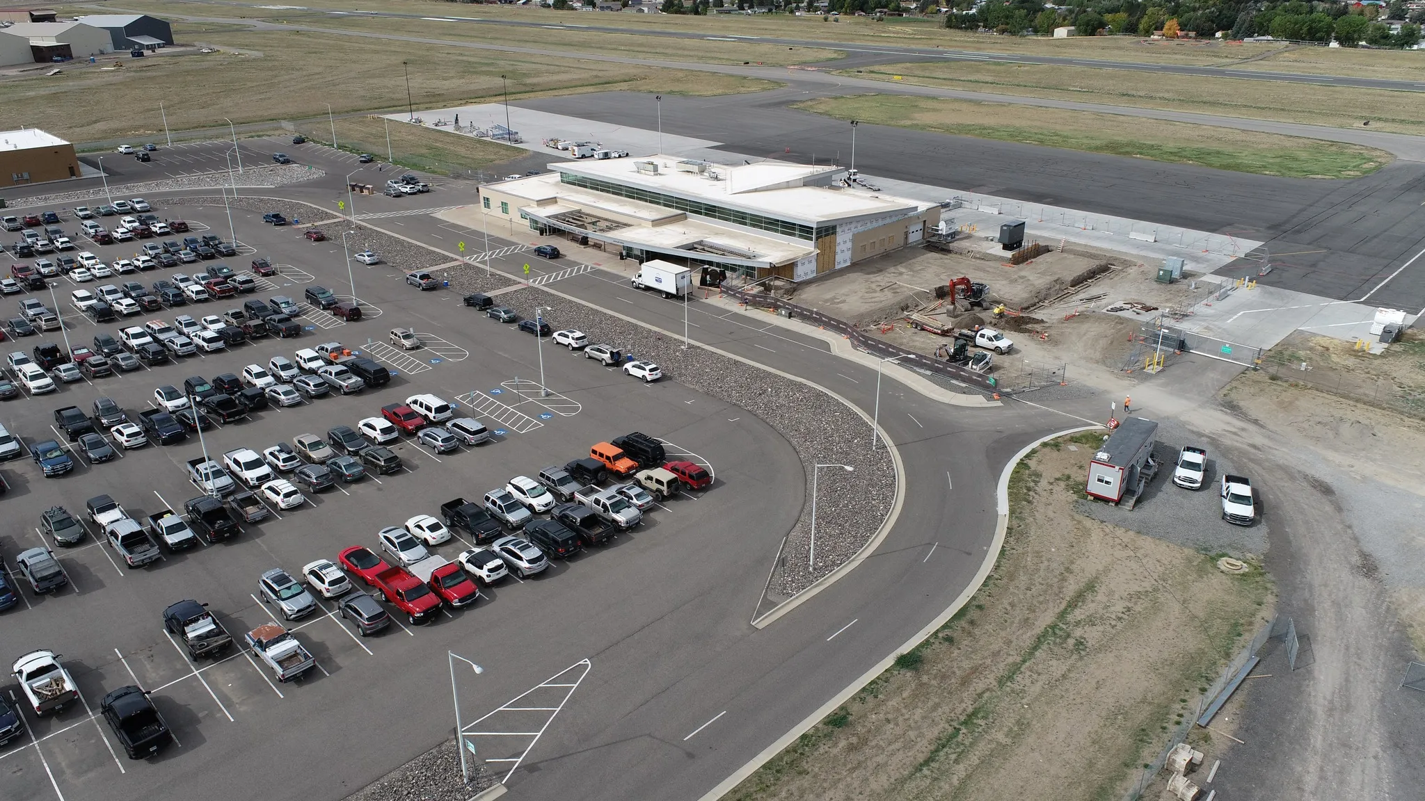 Aerial view of Yellowstone Regional Airport in Cody, Wyoming, showing its terminal, runway, and large parking lot filled with vehicles.