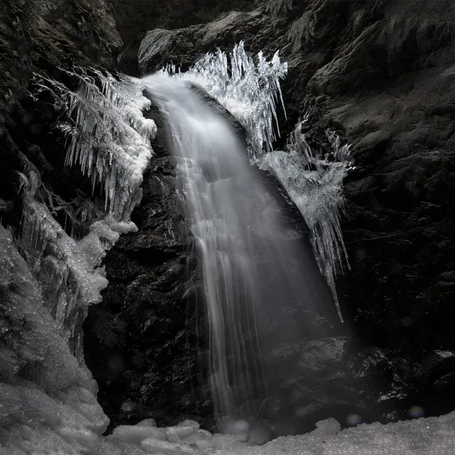 A partially frozen waterfall at Zapata Falls, Colorado, with cascading water surrounded by sharp icicles and dark rock walls.