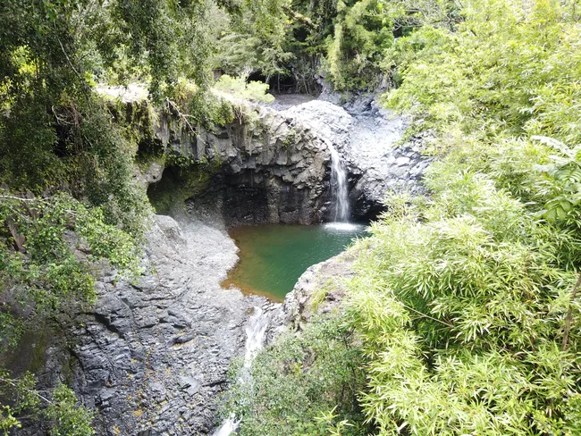 Small waterfall cascading into a circular emerald-green pool surrounded by rocky cliffs and lush vegetation.
