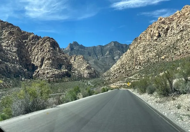 A scenic desert highway winds through rugged red rock canyons under a bright blue sky.