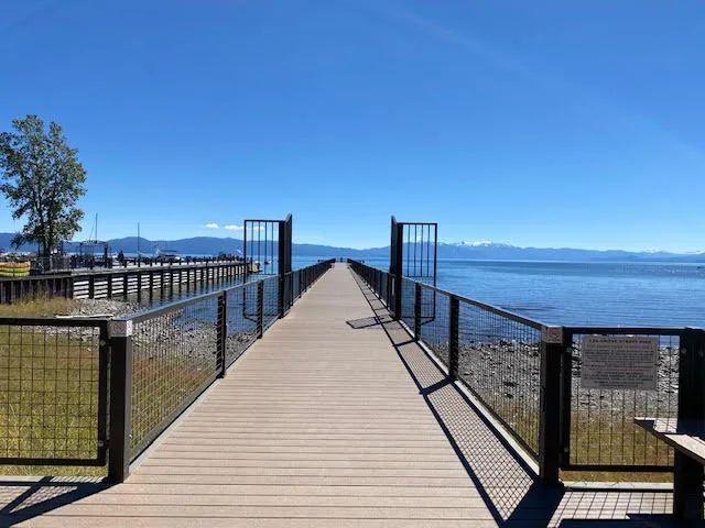 Wooden pier stretching out toward the blue waters of Lake Tahoe with mountains in the distance under a clear sky.