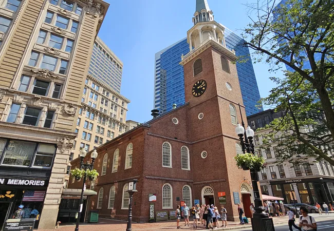 Tourists gather outside the historic red-brick Old South Meeting House, surrounded by modern skyscrapers in downtown Boston.