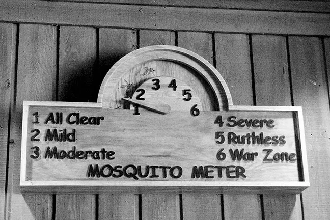 Wooden “Mosquito Meter” sign with a needle gauge showing levels from mild to war zone.