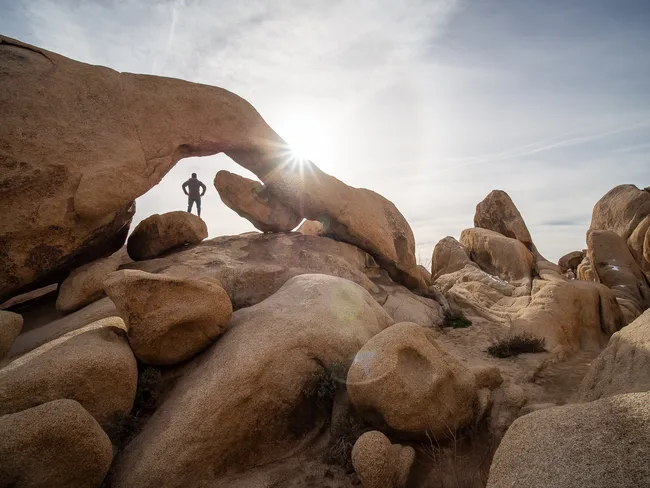 A person standing under Arch rock at Joshua Tree National Park, California