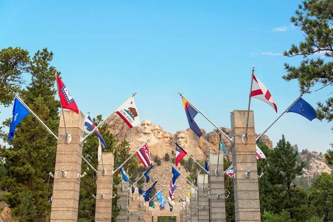 View of Mount Rushmore framed by the Avenue of Flags on a clear day, showcasing state flags and granite columns leading toward the monument.