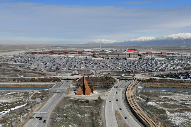 Aerial view of Salt Lake City International Airport with roads, parking lots, and snow-capped mountains in the background.