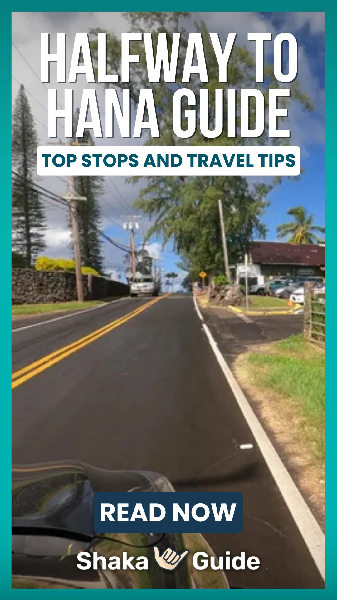 View from a car on the Road to Hana, showing a narrow two-lane street lined with shops, trees, and utility poles in a small Hawaiian town.