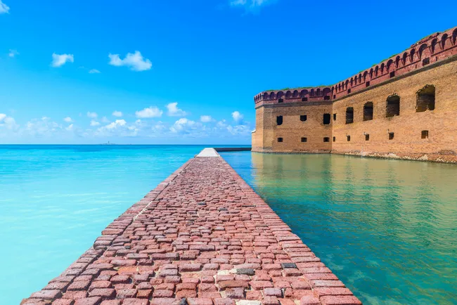The scenic brick moat wall of Fort Jefferson stretches into the turquoise waters under a clear blue sky.
