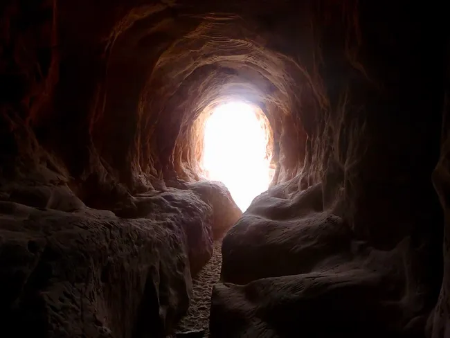 View from inside a narrow sandstone cave in Kanab, Utah, looking toward a bright tunnel opening.