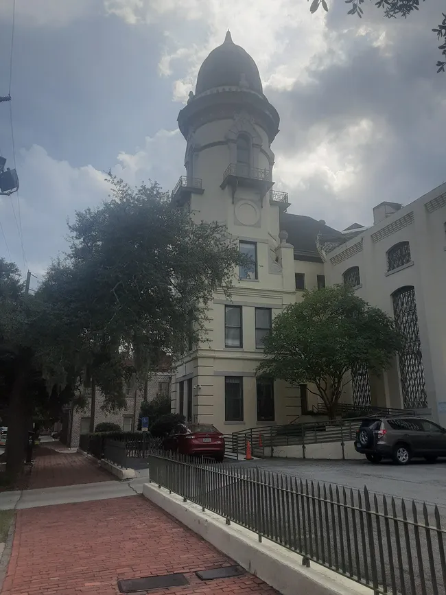 Historic building of the Old Chatham Jail, featuring a distinctive tower and surrounding trees, located on a brick sidewalk.