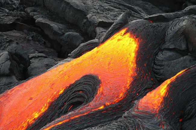Bright orange molten lava flows between hardened black volcanic rock on the Big Island of Hawaii.