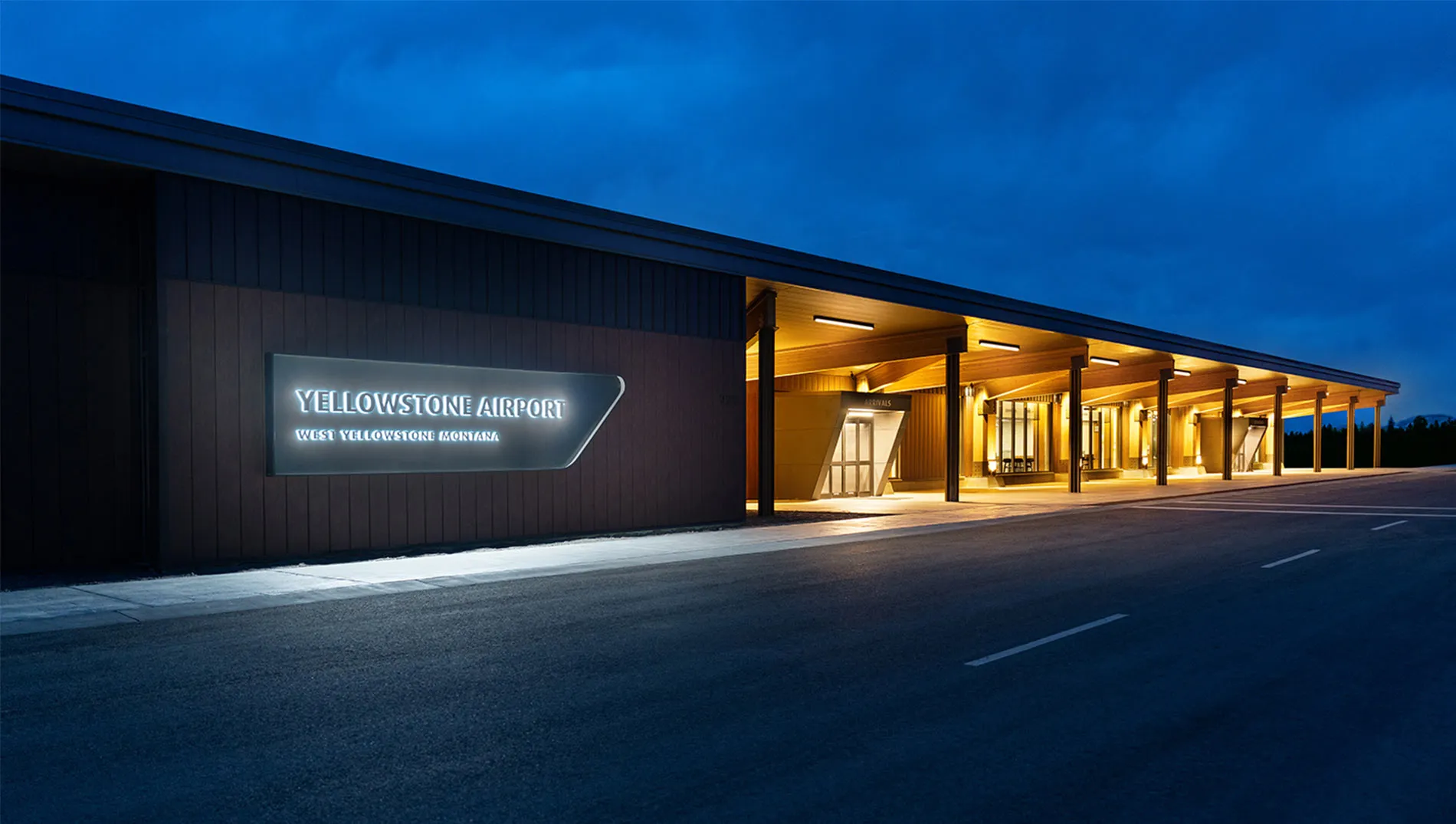 Front exterior of Yellowstone Airport at night, warmly lit entrance with modern wooden design and glowing sign.