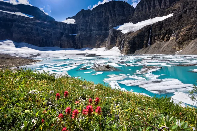 Snow-capped mountains and turquoise glacial lake surrounded by wildflowers in Glacier National Park, Montana.