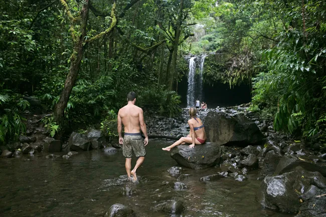 Couple enjoying a lush jungle pool with a small waterfall in the background at Twin Falls, Maui.