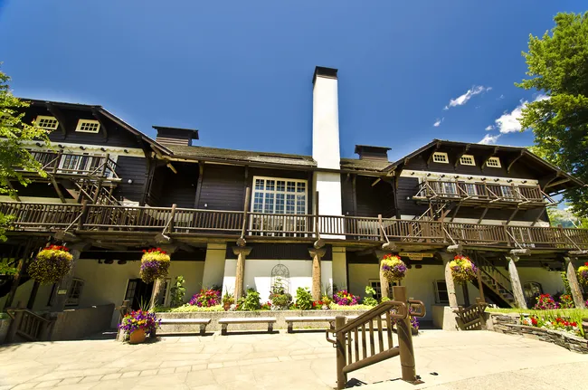 A historic lodge with dark wooden beams, flower baskets, and balconies stands under a clear blue sky.