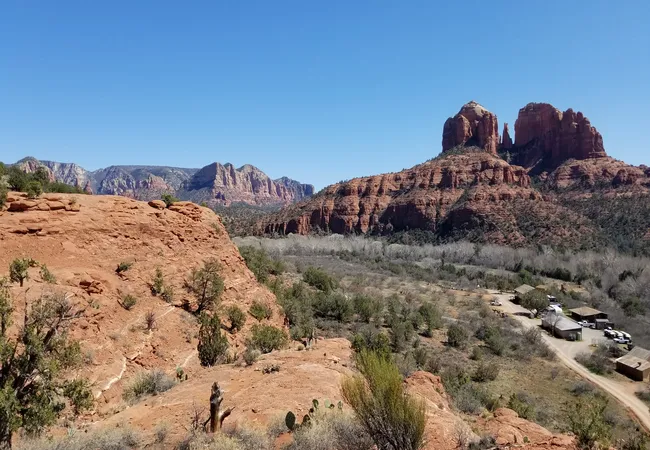 View of Cathedral Rock rising behind Sedona’s Secret Slickrock Trail with red rock formations and desert plants.