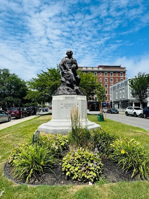 Bronze statue of Nathaniel Hawthorne in Salem park, with the Hawthorne Hotel in the background.