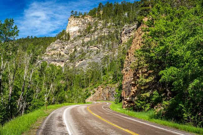 Curving road through Spearfish Canyon Scenic Byway surrounded by steep limestone cliffs and lush green forest.