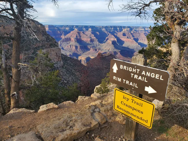Trail signs for Bright Angel and Rim Trail stand at the canyon’s edge, with a caution for icy paths.