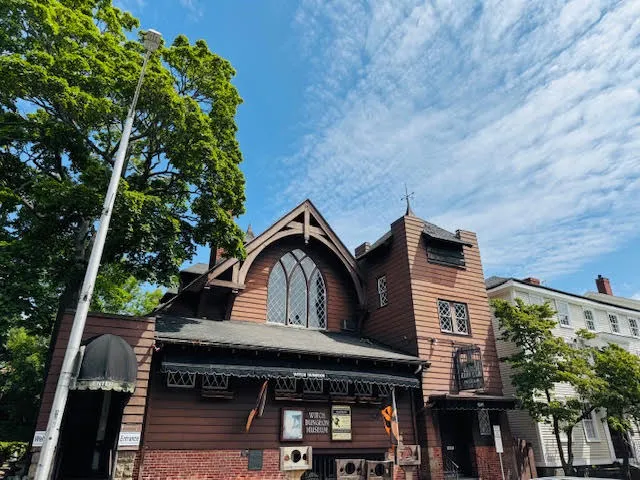 Gothic-style brown wooden building of the Witch Dungeon Museum, featuring arched windows and dramatic rooftop angles.