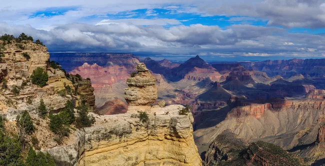 Duck on a Rock viewpoint features a unique rock formation resembling a duck perched on a cliff edge, with layered canyon colors and distant storm clouds adding dramatic flair to the vast Grand Canyon backdrop.