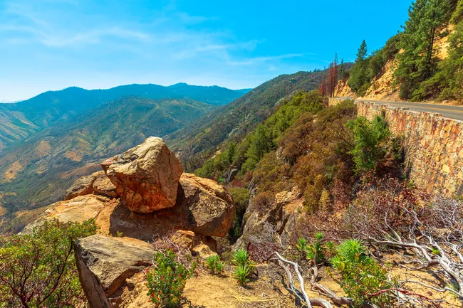 Scenic mountain road winds through Kings Canyon National Park with rocky outcrops and forested slopes.