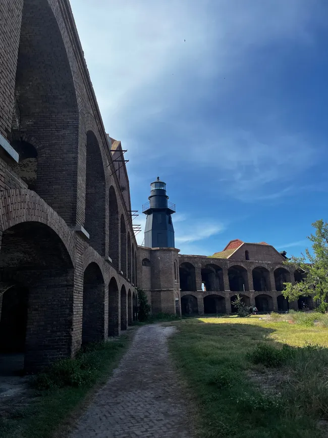 Interior courtyard of Fort Jefferson with a lighthouse in the background under a bright blue sky at Dry Tortugas National Park.