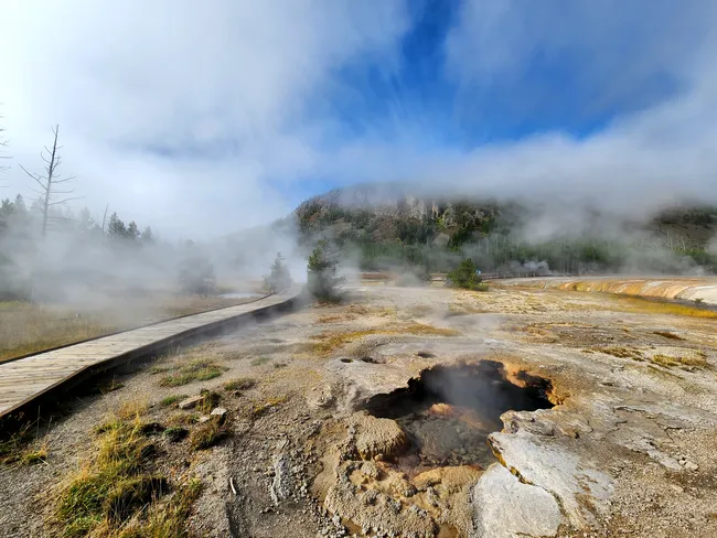 Steaming geothermal vents and a wooden boardwalk in Yellowstone’s Black Sand Geyser Basin.