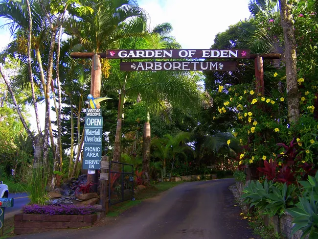 Entrance to the Garden of Eden Arboretum, framed by lush tropical plants and a wooden sign overhead.