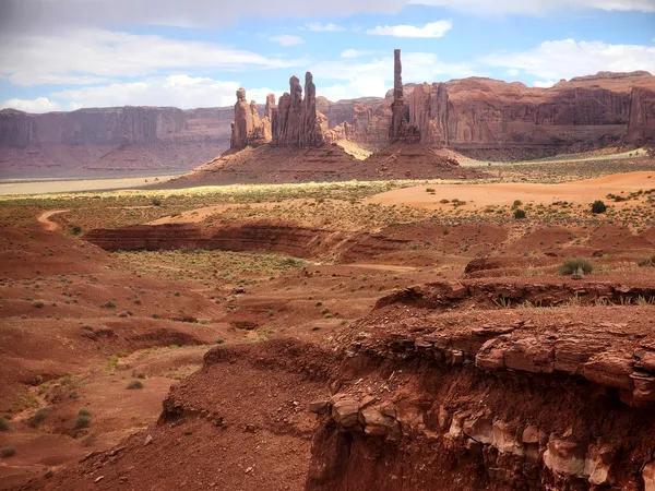Layered red rock formations and eroded desert cliffs with Monument Valley’s iconic spires on the horizon.