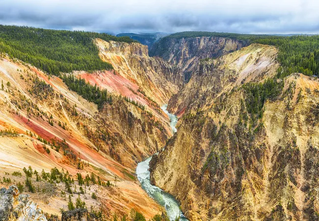 Scenic view of the Grand Canyon of the Yellowstone, with dramatic multicolored canyon walls and the Yellowstone River winding through the deep gorge under a cloudy sky.