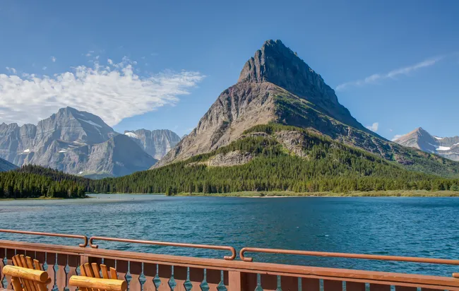 Scenic view of Grinnell Point across Swiftcurrent Lake from a wooden deck with chairs at Many Glacier Hotel.