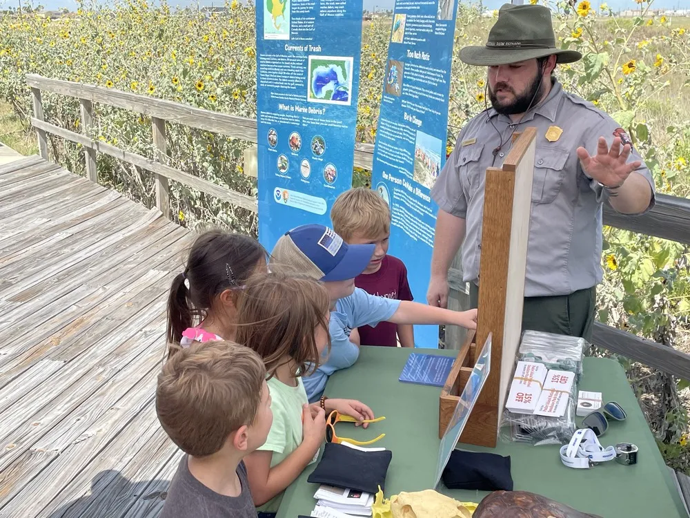 Children engaging in activities at a Junior Ranger program station near nature exhibits on a boardwalk.