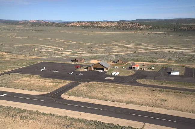 Small regional airport in a desert landscape with several light aircraft on the tarmac and low buildings nearby.