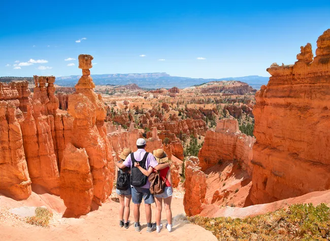 A family views colorful hoodoos and the landscape of Bryce Canyon National Park from a scenic overlook.
