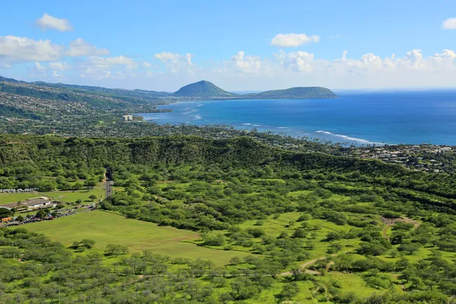Scenic view from Diamond Head Crater, overlooking lush green landscapes, coastline, and distant mountain ridges on Oahu.