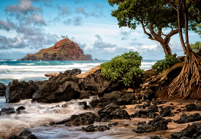 Rocky shoreline at Hamoa Beach in Maui with turquoise waves, lush greenery, and a small island offshore.