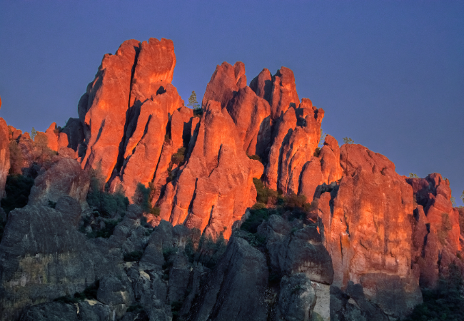 Jagged volcanic spires at Pinnacles National Park glow in vivid orange under the soft light of sunset.