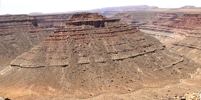 Layered red rock mesa rises sharply from desert canyon floor under hazy midday sun at The Rincon.